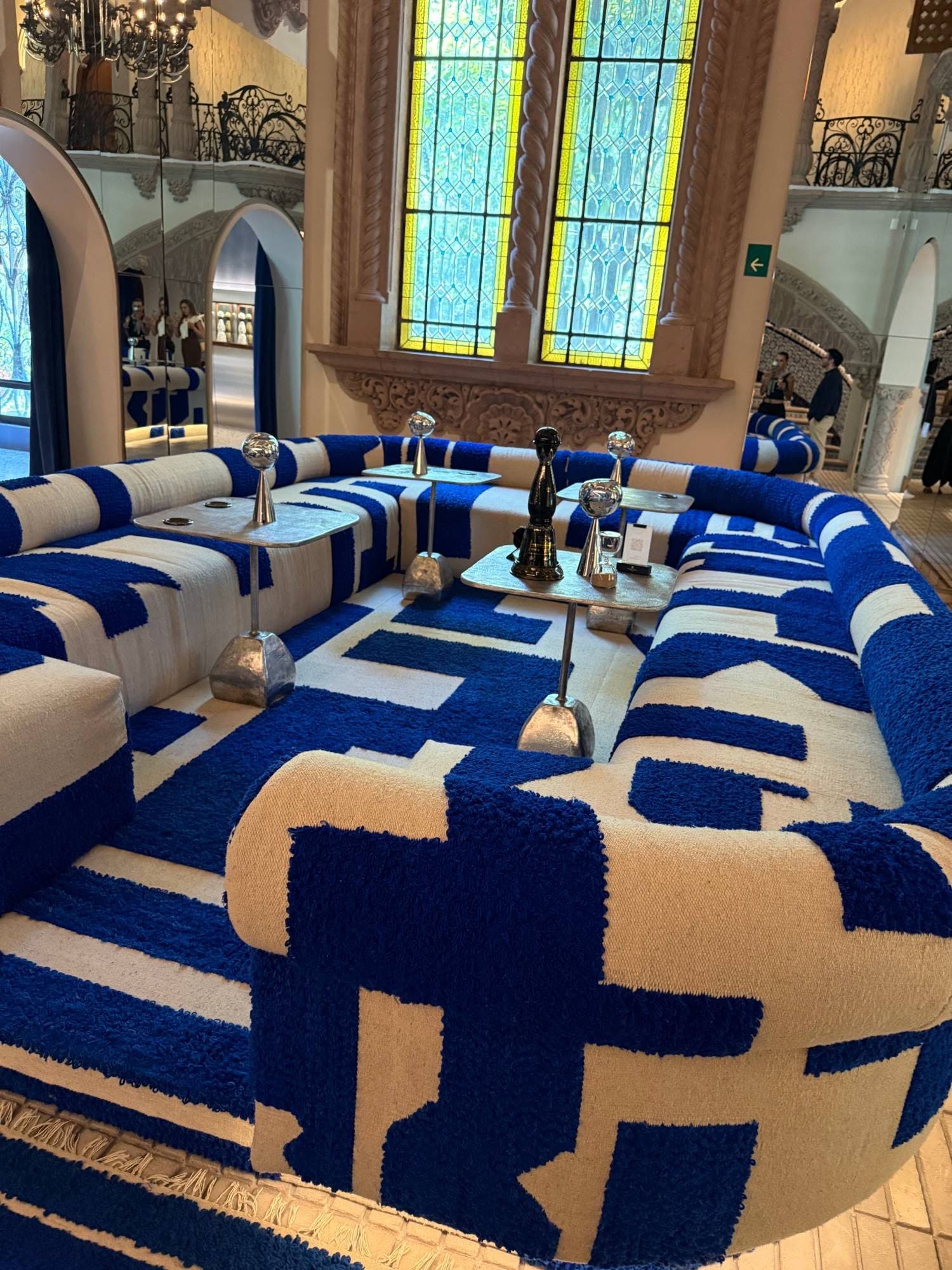 A sculptural blue and cream lounge beneath stained glass and stone columns in a historic mansion