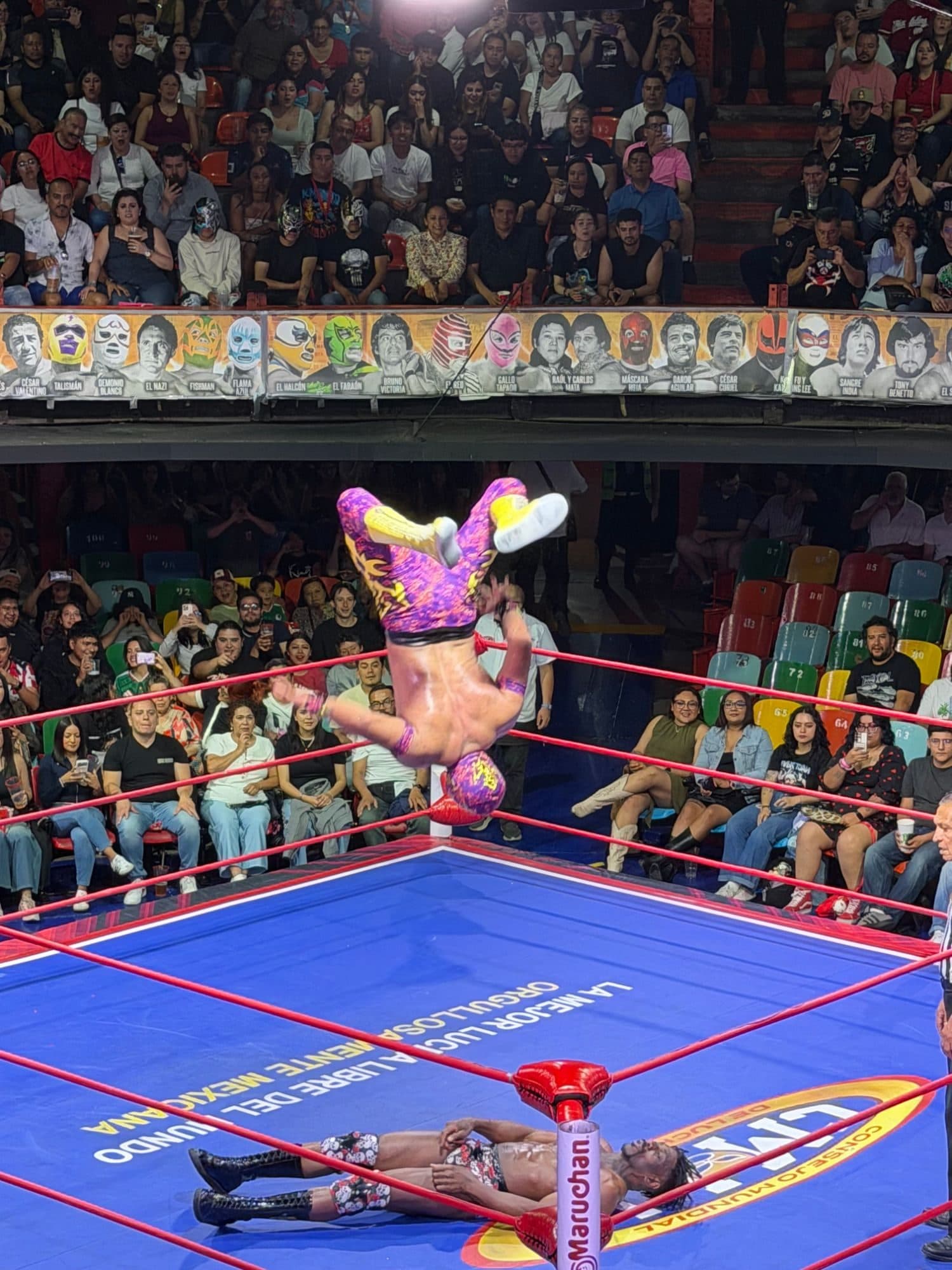 A luchador mid-backflip off the ropes above his opponent at the private lucha libre night