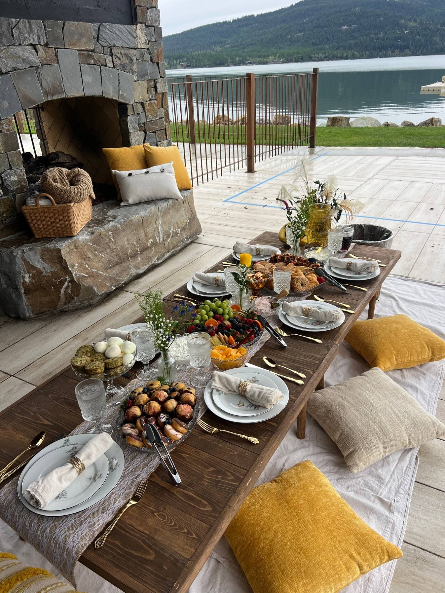 Lakeside farewell picnic at Whitefish Lake: a low wooden table set with pastries and fruit beside a stone fireplace